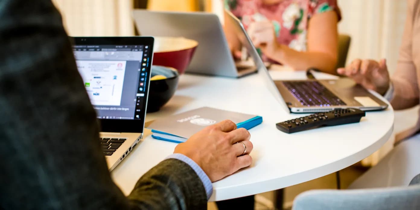 En grupp människor som sitter runt ett bord med bärbara datorer