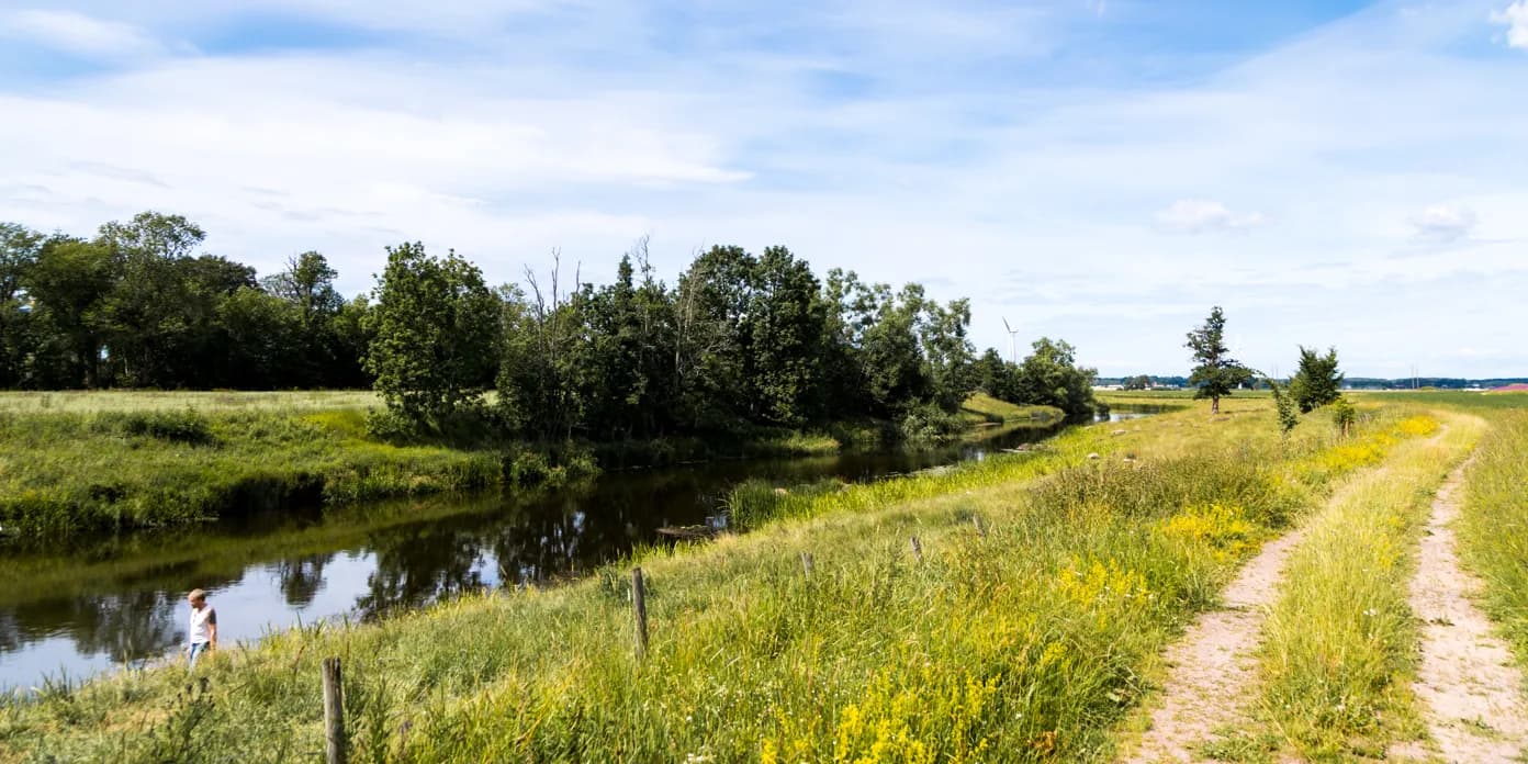 En person som går längs en grusväg intill en flod