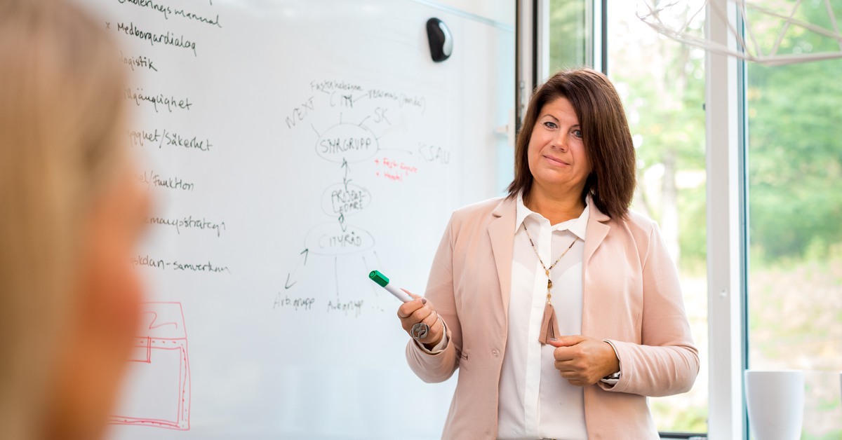 En kvinna som håller i ett möte och står framför en whiteboard. 