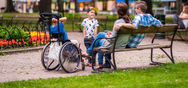 En familj som sitter i en park, ett av barnen sitter i rullstol